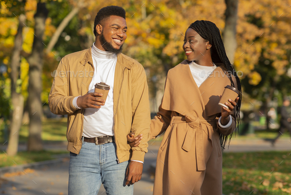 Romantic black couple with coffee walking outdoors in autumn park