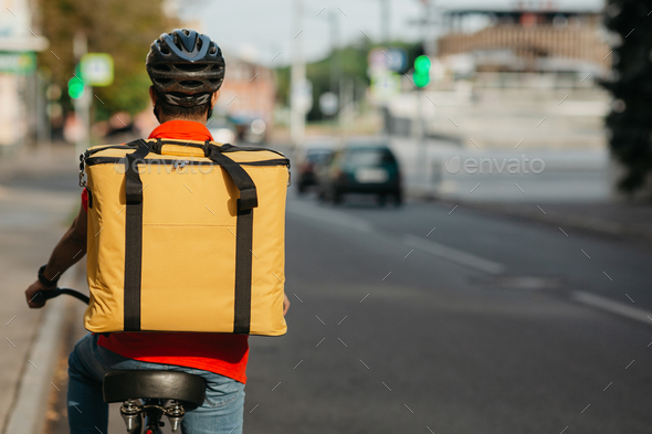City traffic and bicycle delivery service. Courier in helmet, bag, rides on bicycle at road