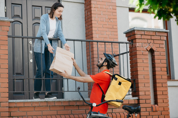 Customer, delivery and courier. Girl takes bag from man with backpack and bicycle, near front door - Stock Photo - Images