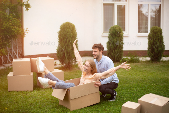 Excited millennial couple playing with carton boxes near their country house on moving day
