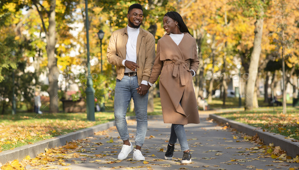 Happy millennial afro couple walking in city park holding hands