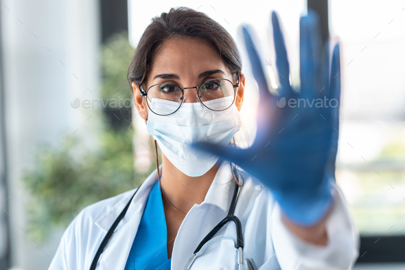 female doctor wearing a hygienic face mask and doing a stop gesture with protective gloves in hands