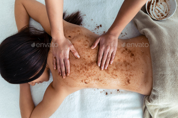 woman applying chocolate cream for body treatment to a pretty woman on the spa center.