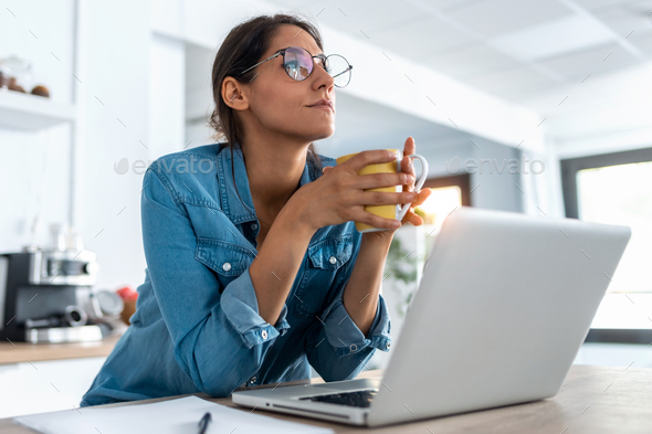 young woman relaxing one moment and drinking coffee while working with laptop