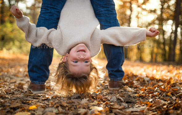Unrecognizable father holding small daughter upside down in autumn forest