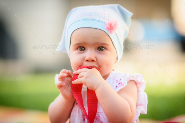 9 months old infant baby girl sits alone in garden grass on colorful blanket. Looking at camera and