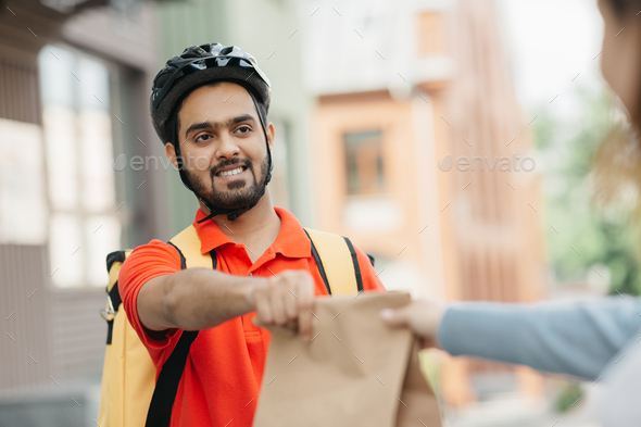 Takeaway restaurant food delivery. Portrait of young courier with beard in protective helmet and