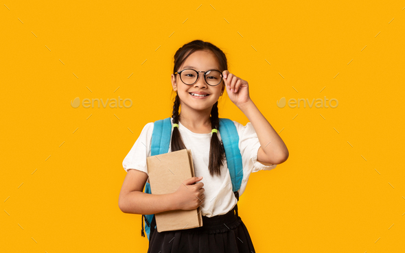 Joyful Korean Kid Girl Holding Book Posing Over Yellow Background