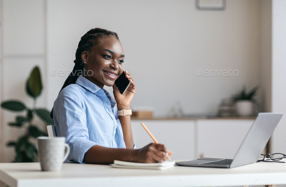 Millennial Black Woman Manager Taking Notes And Talking On Cellphone In Office