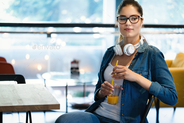 Lifestyle fashion portrait of beautiful woman posing at cafe, drinking fresh healthy tasty juice