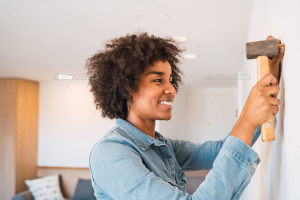 Afro woman hammering nail on the wall at home.