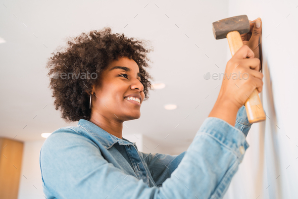 Afro woman hammering nail on the wall at home.