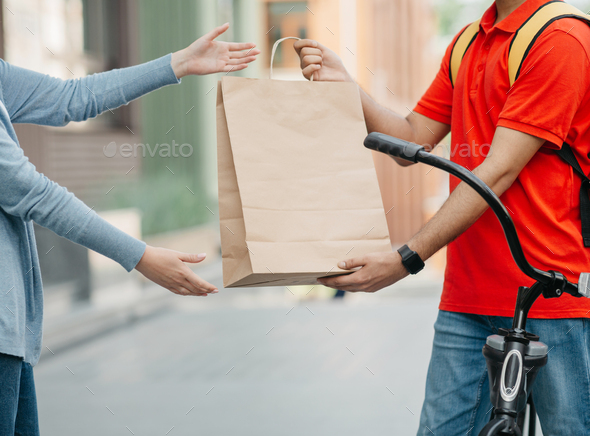Online shopping and delivery by courier on bike. Man with backpack gives paper bag to client