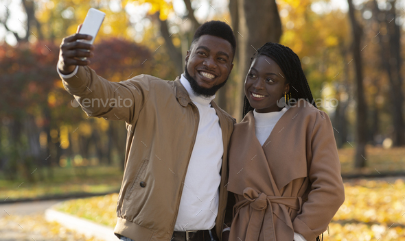 Afro couple in love taking selfie on date in autumn park
