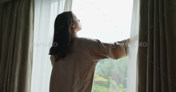 Woman wake up at morning, open the curtain and look around the view outside window
