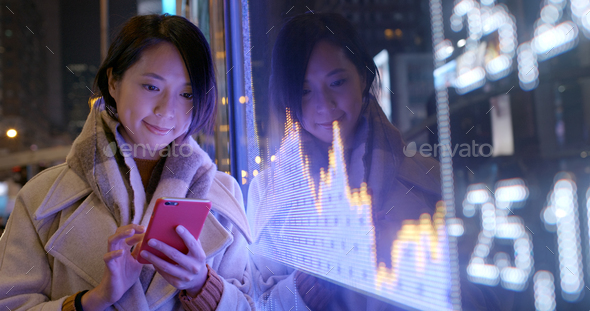 Woman use of mobile phone to check the financial data in the street at night
