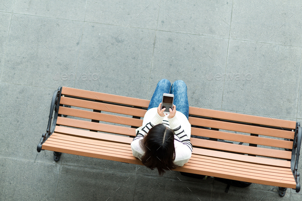 Top view of woman sitting on bench and using mobile phone