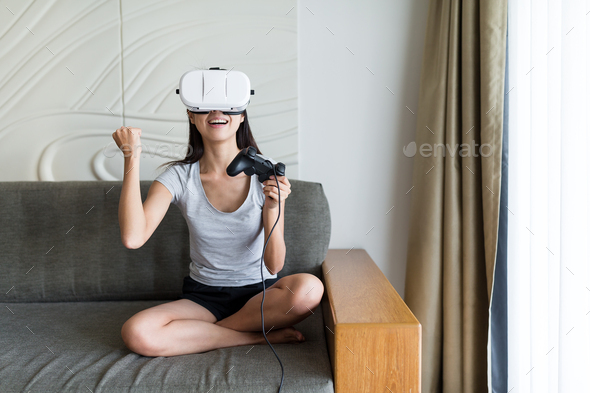 Woman play game with virtual reality device and sitting on sofa