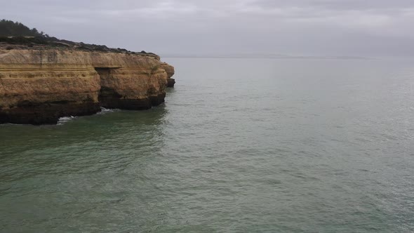 Cliffs in Fontainhas beach of South Portugal seen from the side, Aerial dolly in reveal shot alt