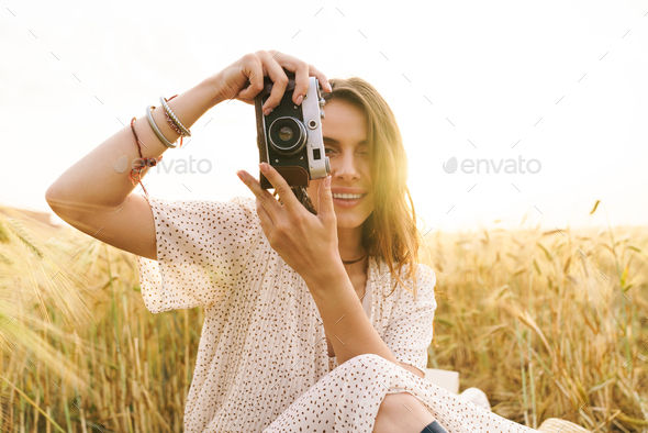 Photo of woman using retro camera while sitting on wheat field