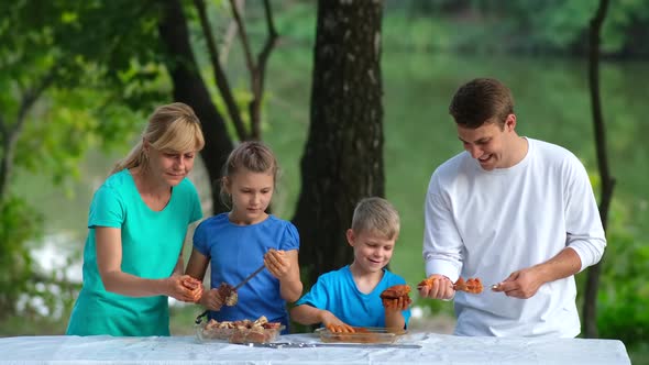 Dad, mom and kids put pickled meat on skewers. Family picnic in the Park.	