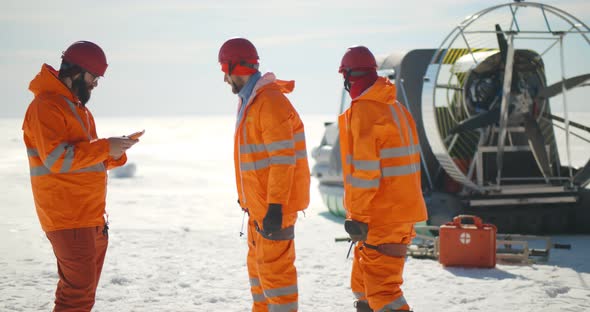 Coast Guard Team Standing on Frozen Lake with Hovercraft on Background alt