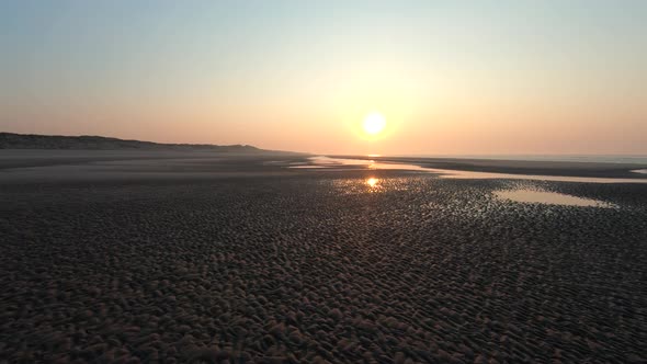 Aerial drone shot of water canals patterns on a beach, towards sunset alt
