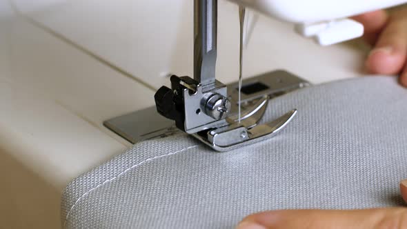 A female hand pushes material through a sewing machine. Close-up of a sewing machine foot. alt