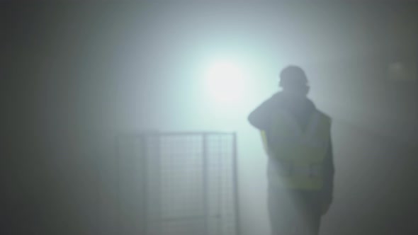 Portrait of the Worker in the Builders Uniform and Helmet on a Black Background in the Spotlight alt