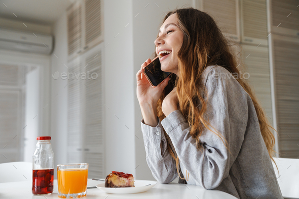 Photo of woman laughing and talking on cellphone while having breakfast