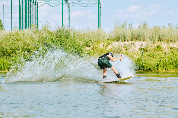 Back view of young active sportsman moving on surfboard and splashing water - Stock Photo - Images