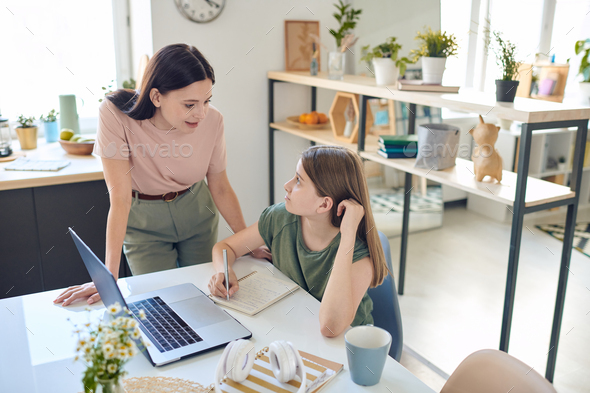 Young mother bending over desk where her teenage daughter studying - Stock Photo - Images