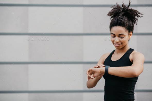 Smiling girl in sportswear checks fitness tracker and happy with result