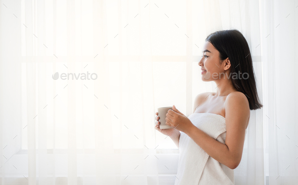 Fresh looking asian woman drinking coffee next to window