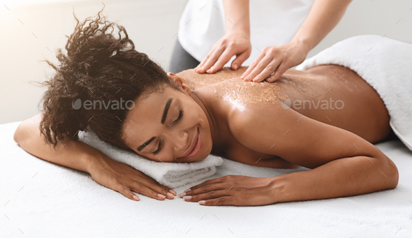 Therapist exfoliating black young woman body at spa