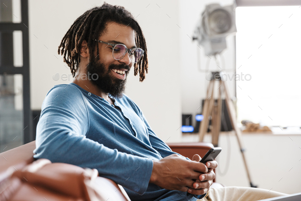Handsome young african man sitting on a leather couch at home