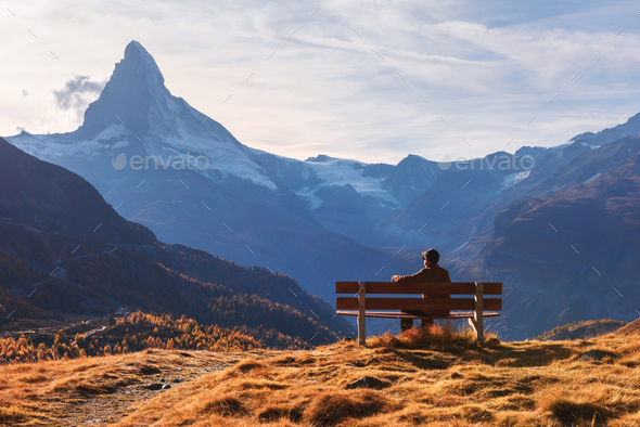 Picturesque view of Matterhorn peak and tourist sitting on wooden bench - Stock Photo - Images
