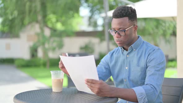 African Man Reading Documents in Outdoor Cafe alt