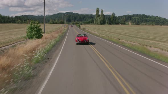 Tracking shot of man driving classic convertible car on country road.  Fully released for commercial