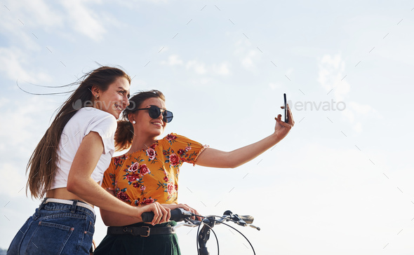 Taking amazing selfie. Two female friends on the bike have fun at beach near the lake
