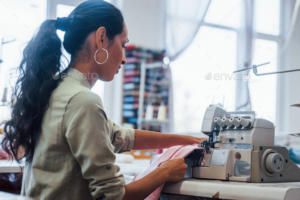 Professional dressmaker woman sews clothes on sewing machine at