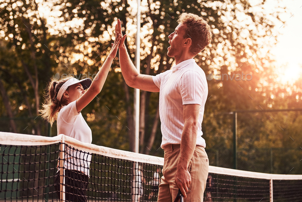 Giving high five. Two people in sport uniform plays tennis together on the court