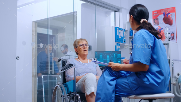 Handicapped senior woman in wheelchair talking with nurse