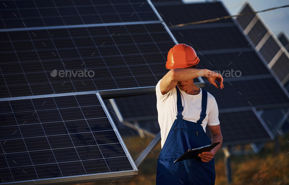 Feels tired. Male worker in blue uniform outdoors with solar batteries at sunny day
