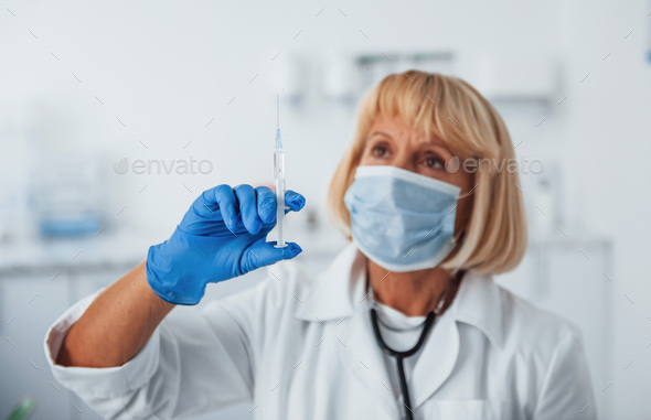 Portrait of senior female doctor in mask with syringe full of liquid