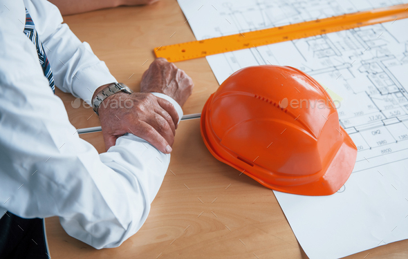 Close up view of senior businessman hands, hard hat and architect project on the table