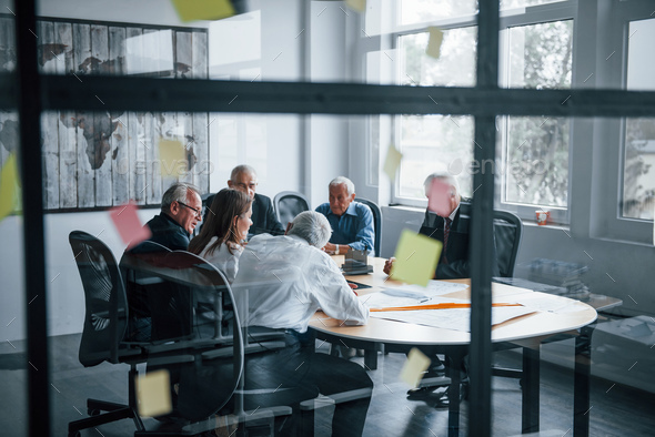 Aged team of elderly businessman architects have a meeting in the office with young woman