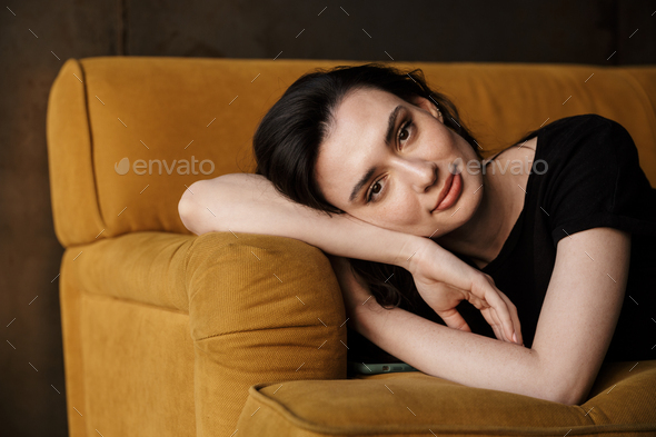 Photo of beautiful young brunette woman lying on couch in apartment