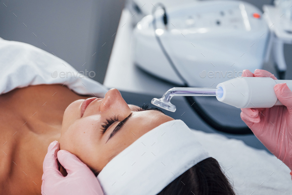 Woman that lying down in spa salon and have face cleaning procedure by using modern device