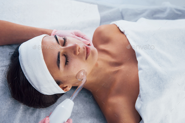 Woman that lying down in spa salon and have face cleaning procedure by using modern device